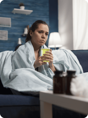 Personne malade enroulée dans une couverture tenant un verre de jus.