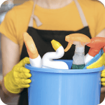 Personne portant des gants jaunes et un tablier tenant un seau rempli de produits de nettoyage.