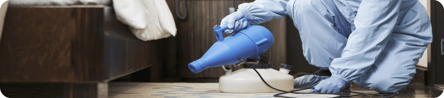 Technicien en combinaison de protection traitant un intérieur contre les insectes nuisibles.